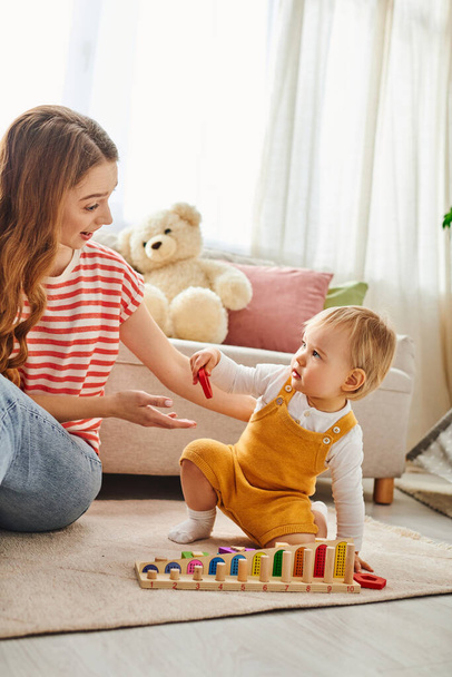 Eine junge Mutter beschäftigt sich mit ihrer kleinen Tochter und spielt gemeinsam auf dem Fußboden in einem warmen und liebevollen Moment zu Hause. - Foto, Bild