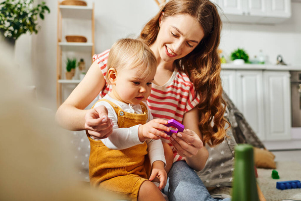 A young mother and her toddler daughter engrossed in game, sharing a moment of technology-driven playtime at home. - Photo, Image