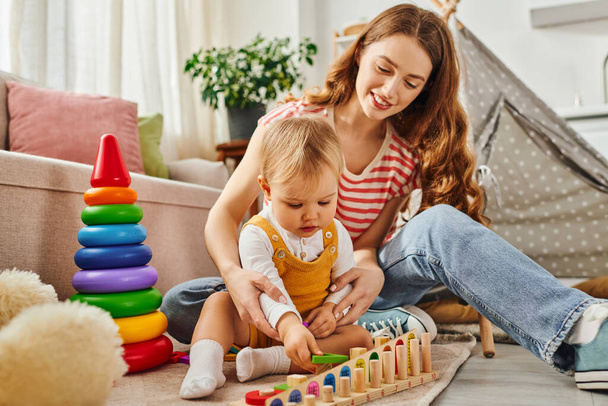 Nuori nainen onnellisesti harjoittaa hänen lapsi tytär, leikkii lattialla kotona. - Valokuva, kuva