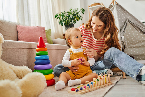 Egy fiatal anya örömmel vesz részt a kislányával, játékosan kölcsönhatásba lép egy meleg és hangulatos nappaliban.. - Fotó, kép