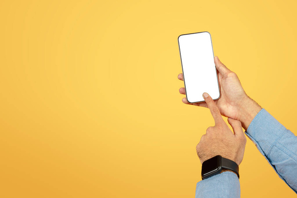 Dłoń prezentująca smartfona z pustym, edytowalnym ekranem na ciepłym żółtym tle do makiet - Zdjęcie, obraz
