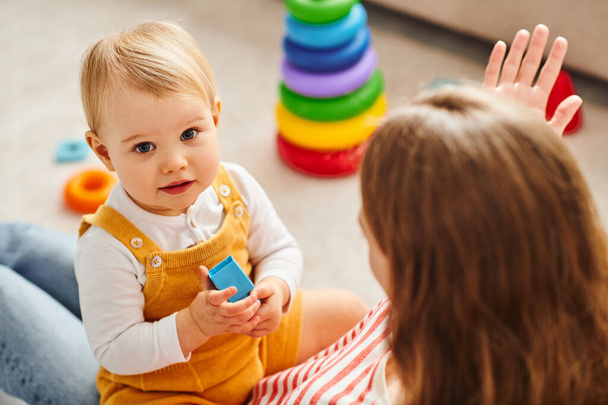 Een baby meisje en haar moeder communiceren, spelen vrolijk op de vloer thuis. - Foto, afbeelding
