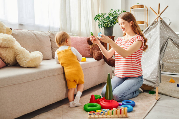 Uma jovem mãe e sua filha criança rindo e brincando em uma sala de estar calorosa e convidativa. - Foto, Imagem