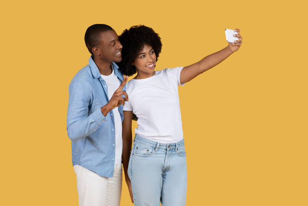 Afroamericani giovane coppia con abiti alla moda è in posa per un selfie, catturando un momento gioioso insieme - Foto, immagini