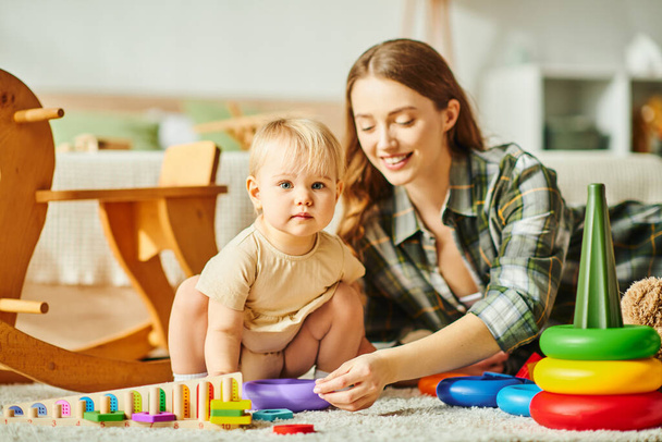 Eine fröhliche junge Mutter interagiert mit ihrer kleinen Tochter auf dem gemütlichen Fußboden ihres Hauses. - Foto, Bild