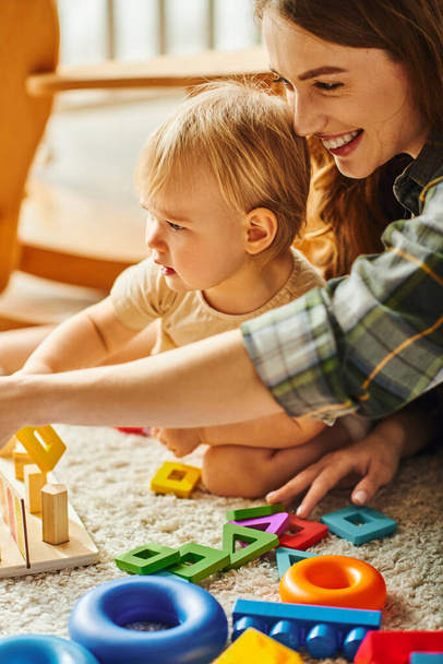 Eine junge Mutter und ihre kleine Tochter spielen zu Hause fröhlich mit Spielzeug auf dem Boden. - Foto, Bild