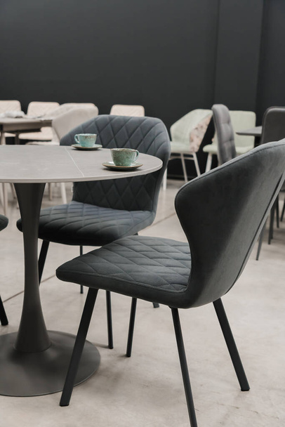 Table en bois gris combiné avec des chaises en bois gris avec revêtement en tissu doux. Il y a des tasses et des soucoupes en porcelaine bleue sur la table - Photo, image