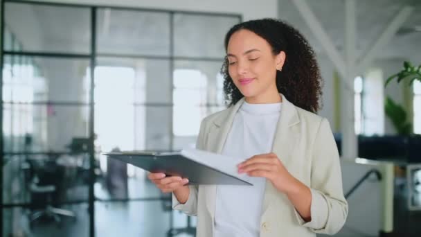 Successful elegant pretty multiracial woman, successful employee of a company, female teacher, standing with documents folder in hands in a modern creative office, looks at camera, smiles friendly - Footage, Video