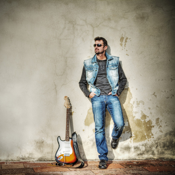 man and guitar against a grungy wall in hdr - Foto, Imagen