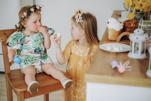 イースターの朝に2人の姉妹がお菓子を食べる. 家族と一緒に家でイースターを祝う. - 写真・画像