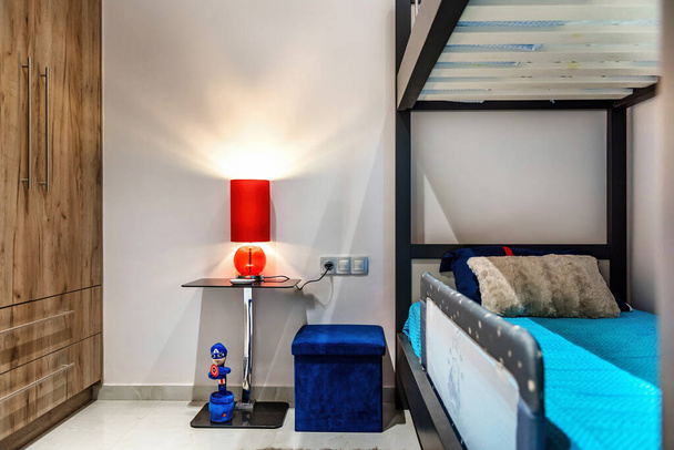 Una camera da letto creativa per bambini con un letto a castello abbinato a un comodino elegante, accentuato da una lampada rossa audace per aggiungere fascino e funzionalità. Perfetto per l'ispirazione di interior design - Foto, immagini