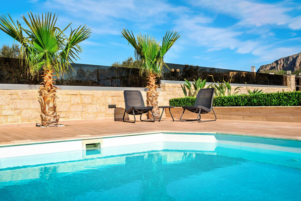 Terraza soleada Villa: Sillas cómodas con vistas a la piscina privada, creando un ambiente sereno en un día soleado. Perfecto para un concepto de villa, esta terraza soleada ofrece relajación y vida de lujo - Foto, Imagen
