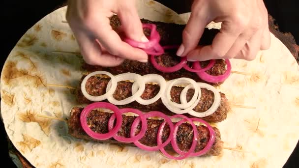 Kebab: grilled sausages on minced meat skewers with pita bread on a wooden board. The chef decorates the dish with white and red pickled onions. Top view. Oriental cuisine - Footage, Video