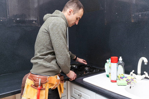 Um engenheiro de gás repara um fogão a gás na cozinha. A chamada do mestre do gás para a casa. .. Foto de alta qualidade - Foto, Imagem