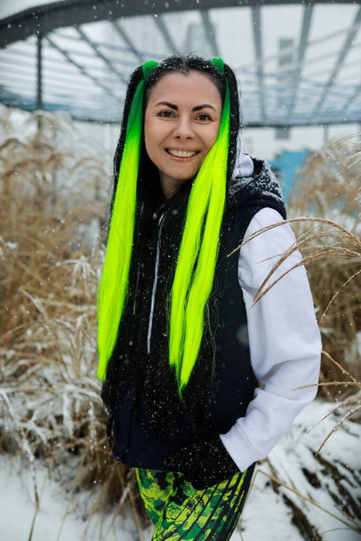 Una donna con i capelli verdi vivaci si trova in mezzo a un paesaggio innevato, i suoi capelli sorprendenti contrastano con la neve bianca. Guarda avanti, incarnando un senso di forza e resilienza al freddo - Foto, immagini