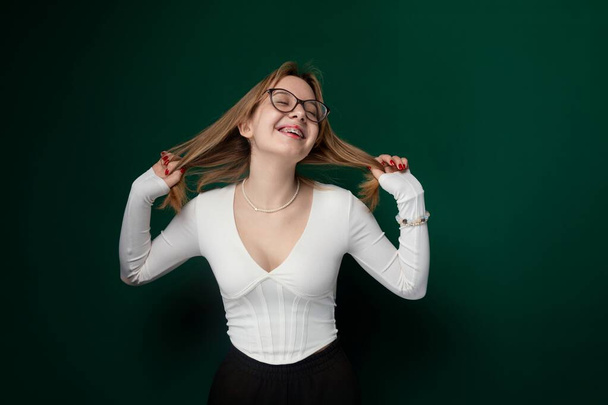 Eine Frau mit Brille ist in einem knackig weißen Hemd zu sehen, die in schlichter, aber stilvoller Pose vor schlichtem Hintergrund steht.. - Foto, Bild