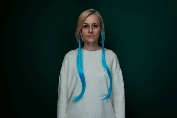 Kobieta z niebieskimi włosami stoi przed zielonym tłem. Jej włosy wyróżniają się na tle, tworząc uderzający kontrast. Kobieta wydaje się pewny i stylowy w jej unikalny - Zdjęcie, obraz