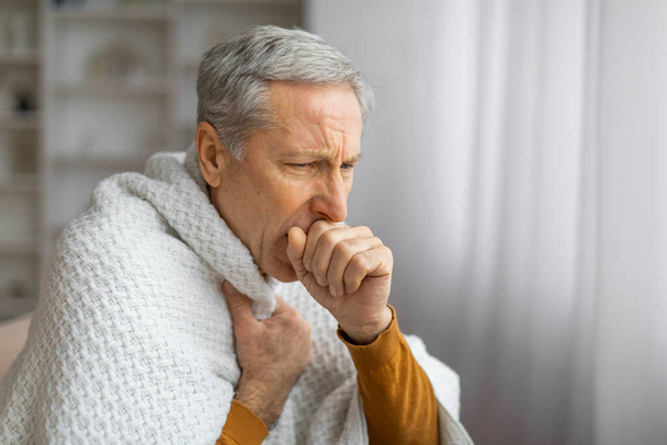 Sağlığı yerinde olmayan yaşlı bir erkek battaniyeye sarınır, duruşu ve ifadesi hastalık ya da rahatsızlığı gösterir, sağlık sorunlarını betimler. - Fotoğraf, Görsel
