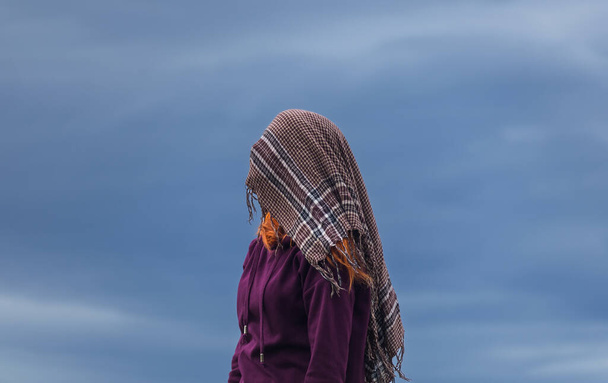 Portrét mladé ženy zakryté šátkem proti modrému mraku. Koncept bez tváře - Fotografie, Obrázek