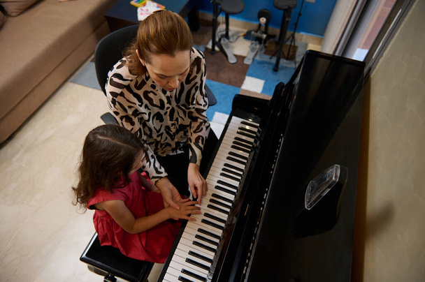Vista desde arriba de un caucásico agradable maduro profesor de música femenina, músico pianista enseñando piano, explicando a una niña estudiante la posición correcta de los dedos en las teclas de piano. - Foto, Imagen