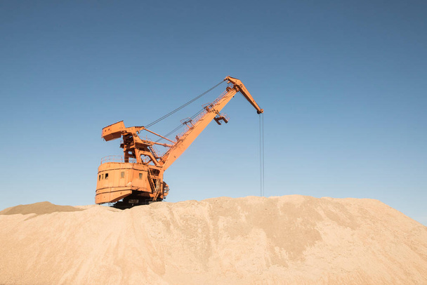 Портовый промышленный кран при выгрузке речного песка в ясный солнечный день - Фото, изображение