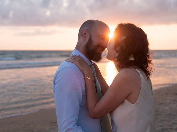 Un couple s'embrasse sur une plage, le coucher de soleil derrière eux jette une lueur chaude. - Photo, image