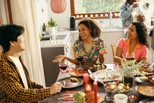 Mosolygó barátok csoportja, akik otthon élvezik a beszélgetést és bort isznak a karácsonyi partin - Fotó, kép