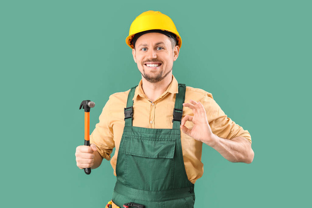 Carpintero macho con martillo que muestra OK sobre fondo verde - Foto, imagen