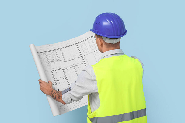 Молодой инженер-мужчина с чертежом на синем фоне, вид сзади - Фото, изображение
