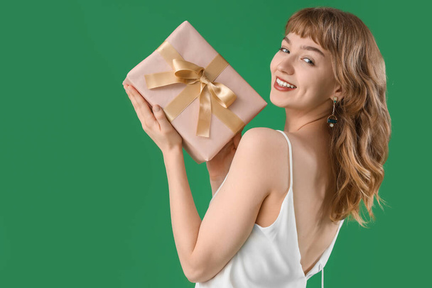 Beautiful young woman with gift box on green background - Photo, Image