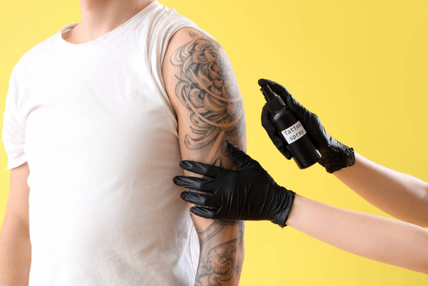 Tatuaje maestro pulverización brazo del hombre contra el fondo amarillo, primer plano - Foto, imagen