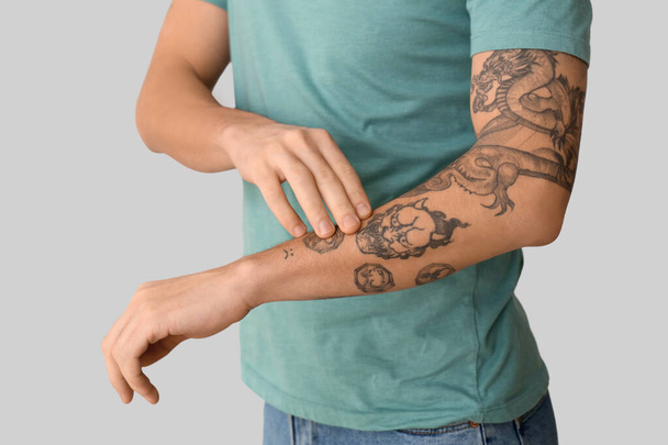 Jovem com braço tatuado no fundo claro, close-up - Foto, Imagem