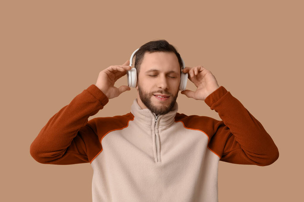 Jovem em fones de ouvido modernos em fundo marrom - Foto, Imagem