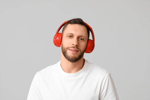 Молодий чоловік в сучасних навушниках на сірому фоні - Фото, зображення