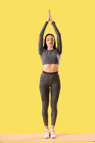Portrait of sporty young woman practicing pilates on yellow background - Photo, Image