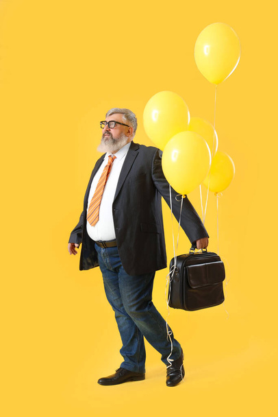 Starší podnikatel s aktovkou a balónky na žlutém pozadí - Fotografie, Obrázek