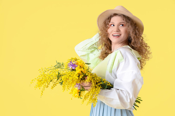 Pretty young woman with bouquet of beautiful flowers on yellow background - 写真・画像