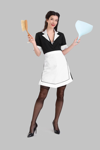 Beautiful pin-up chambermaid with cleaning brush and scoop on grey background - Photo, Image