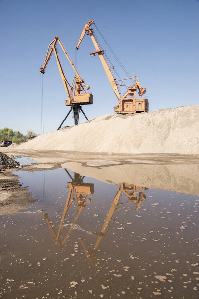 Портовые промышленные краны при выгрузке речного песка в ясный солнечный день - Фото, изображение
