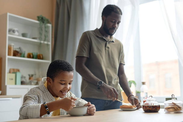 Portret Afroamerykańskiej rodziny z ojcem i synem jedzący razem śniadanie przy stole kuchennym przestrzeń do kopiowania - Zdjęcie, obraz