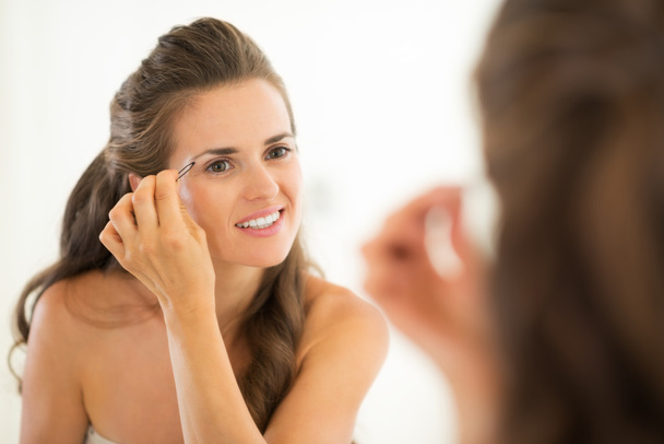 Happy young woman shaping eyebrows in bathroom - Photo, Image