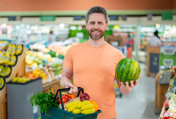 Man with grocery basket shopping at supermarket. Grocery store, shopping basket. Banner with man for grocery food store or supermarket. Man choosing food in store or grocery store - Foto, Imagen