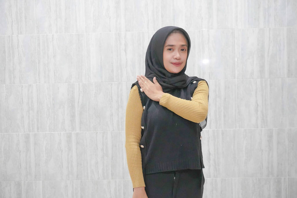 Expression of an Asian Indonesian woman wearing a black hijab with yellow sleeves - Photo, Image