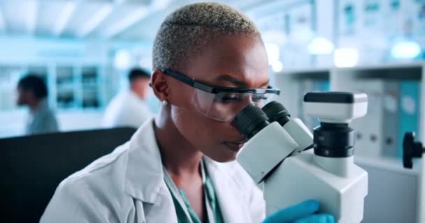 Ciencia, investigación y mujer negra al microscopio comprobando los resultados en la prueba farmacéutica en laboratorio. Gafas, seguridad y científicos que estudian la muestra con innovación médica para el desarrollo de vacunas. - Imágenes, Vídeo