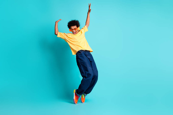 Full length photo of eccentric guy dressed yellow t-shirt sunglass headphones stand on tiptoes isolated on turquoise color background. - Fotografie, Obrázek