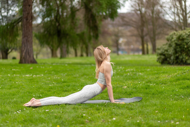 Mujer haciendo yoga en el parque, ejercicio de cobra. - Foto, imagen