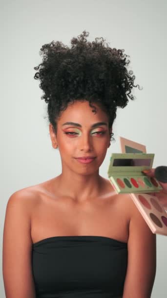 Profesionální make-up master aplikuje barvu na mladý model s kudrnatými vlasy. Svislý, pomalý pohyb, zavření. - Záběry, video