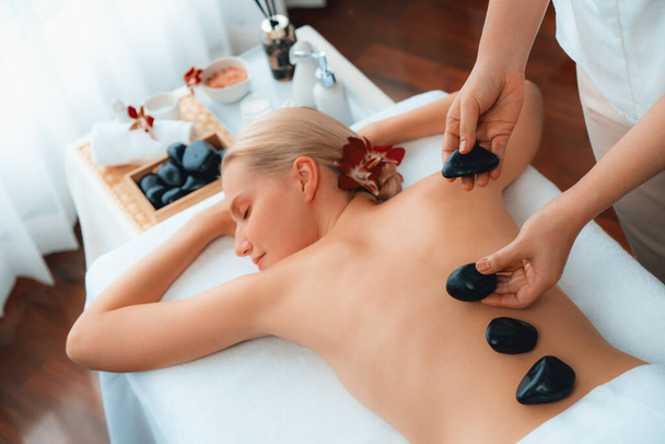 Hot stone massage in spa salon in luxe resort met daglicht sereniteit ambient, gelukzalige vrouw klant genieten spa basalt steen massage glijden over het lichaam met rustgevende warmte. Stil maar. - Foto, afbeelding
