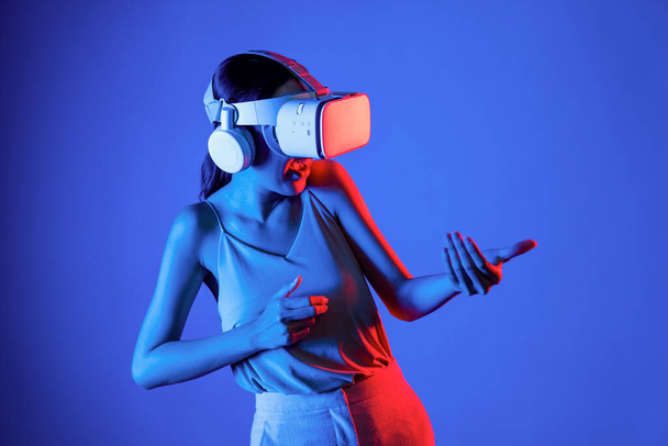 Slimme vrouw die VR-headset draagt die metaverse verbindt, toekomstige cyberspace-community-technologie. Elegante vrouw met behulp van handen commanderen virtuele pistool serieus het spelen van schietspellen. Hallucinatie. - Foto, afbeelding