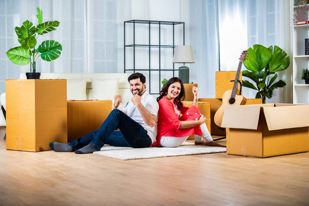 Концепция домашнего переезда, индийская молодая пара, сидящая на полу гостиной с картонными коробками - Фото, изображение